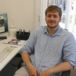 Image of CTH intern, Tommy Fenwick smiling while sitting at his work desk