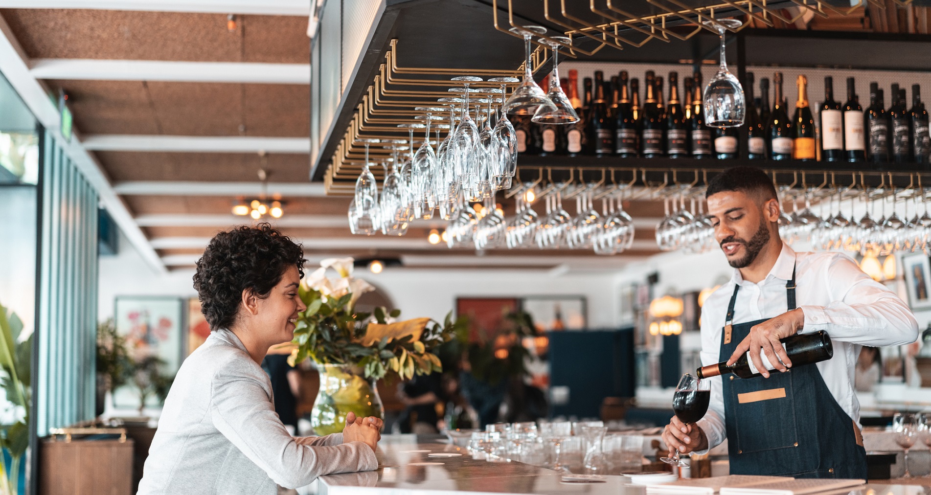 Young male bartender pouring red wine in a luxury bar for a happy female customer.