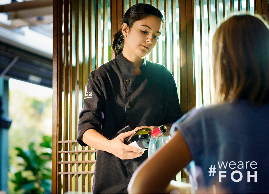 A waitress who has taken the Level 2 Certificate in Professional Restaurant Front of House Service is demonstrating her skills by pouring a bottle of wine for a guest.