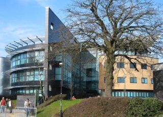 The Swansea University campus main building. This picture was taken on a bright clear day with students walking past the front.